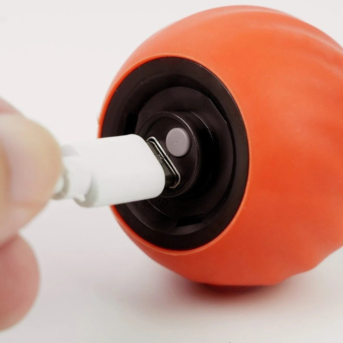 Close-up of a person plugging a USB-C charger into the orange Zoomie Tail interactive cat ball for recharging.